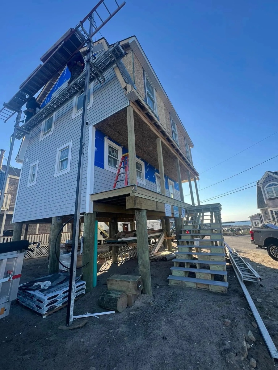 Three-story coastal modular home mid-construction — Tyvek house wrap installed, scaffolding in place, South Shore MA