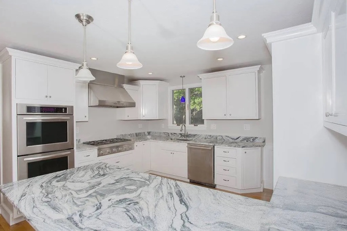 Custom modular home interior kitchen — white shaker cabinets, marble waterfall island, gas range, stainless appliances