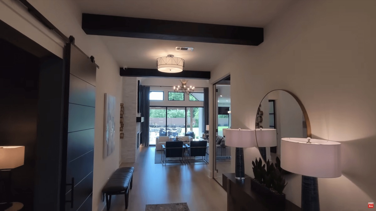 Custom modular home interior — entry view through open living area with exposed beam ceiling, sliding barn door, and large picture windows